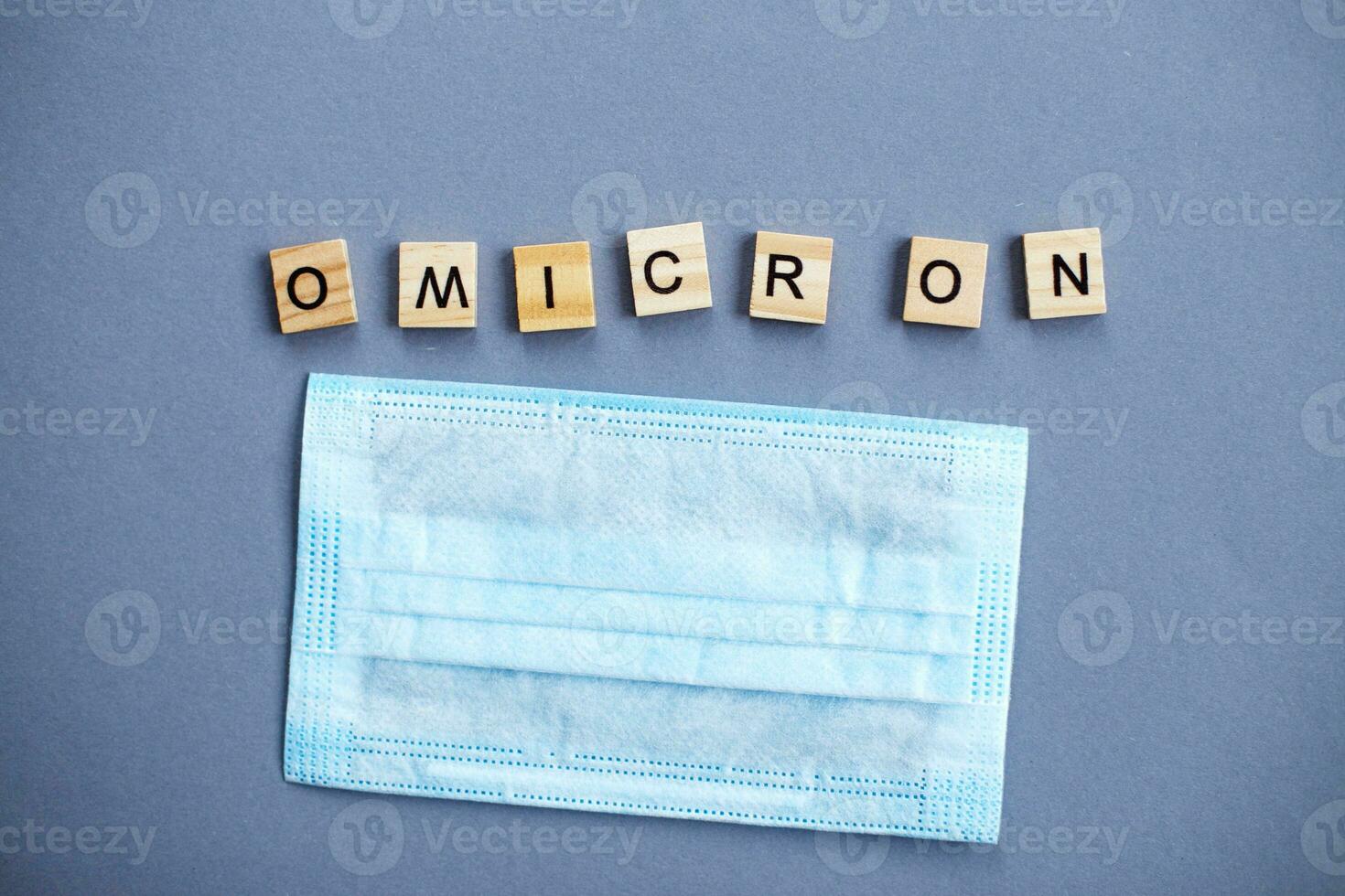 word omicron made by wooden blocks with medical mask on gray background. photo