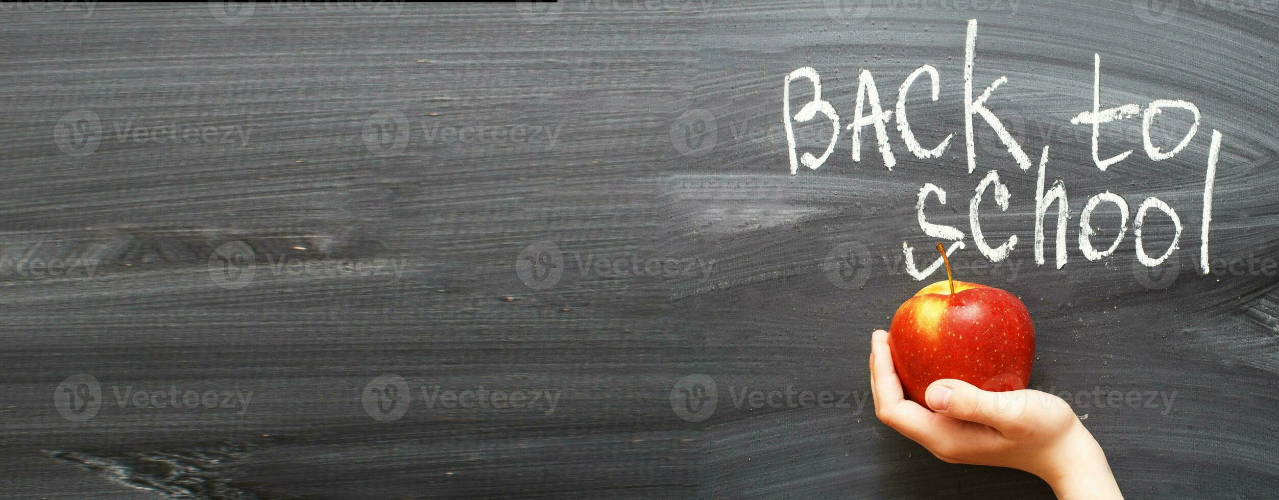 child's hand holding an apple near chalkboard. Back to school concept background. banner photo