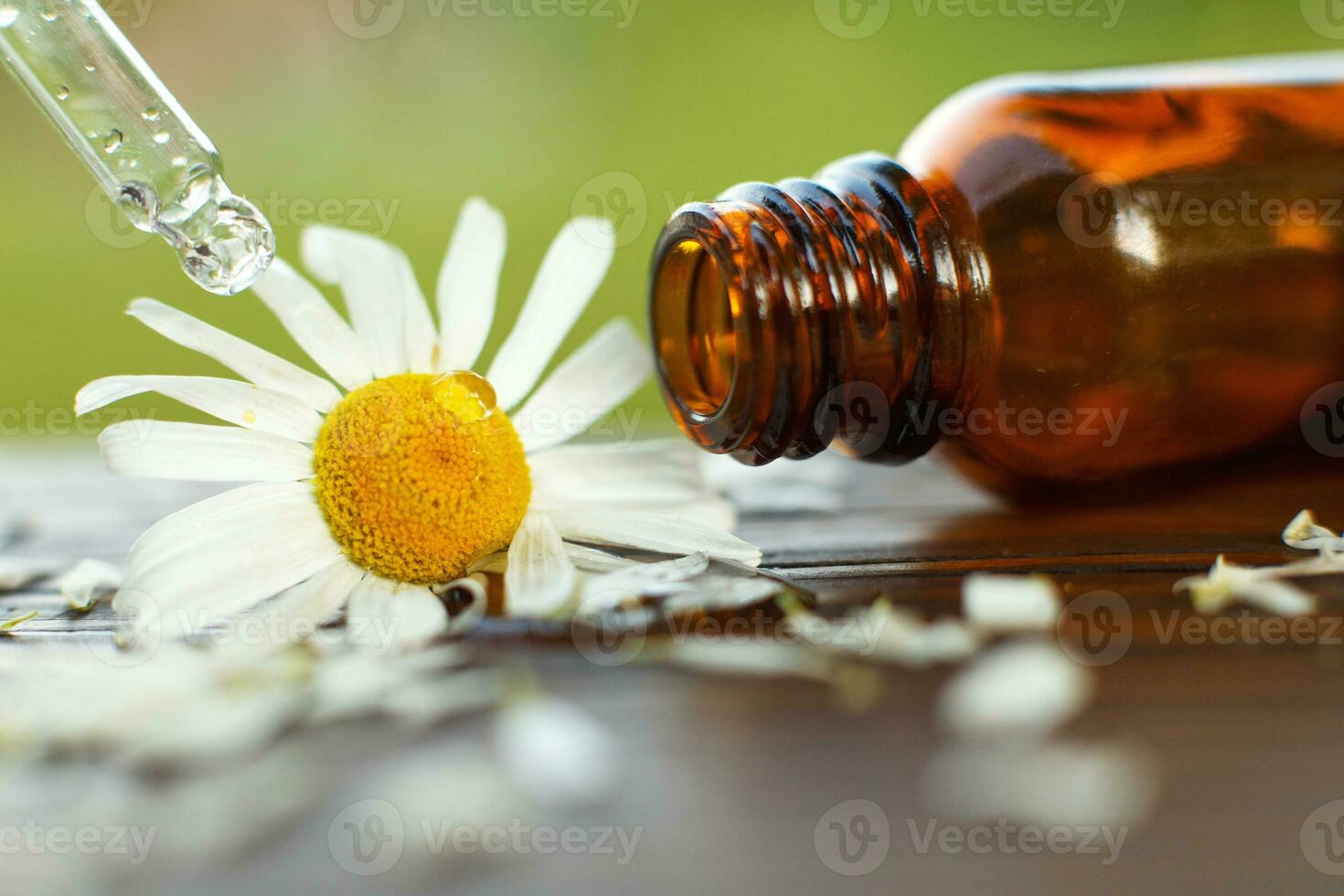 Chamomile essential oil brown glass bottle with a pipette with drop on a wooden table outdoor. photo