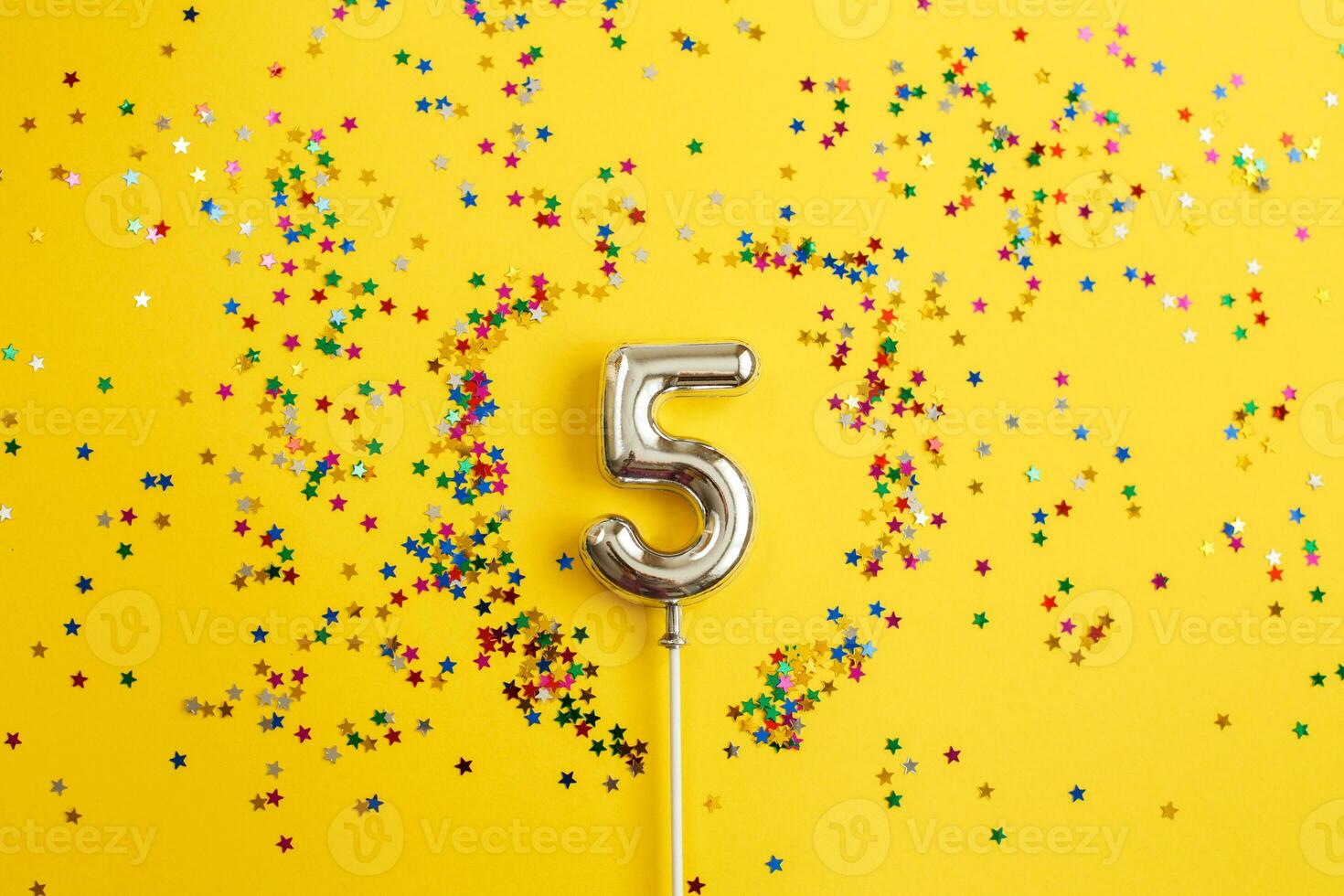 five years birthday party. number five with multicolored confetti in the form of stars on a yellow background photo
