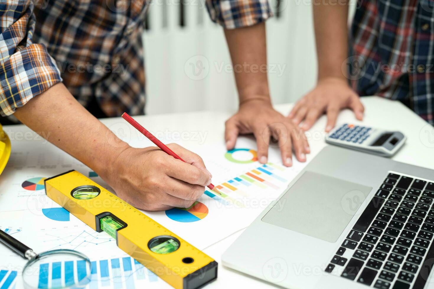 Asian engineer and partner team learn and talk with house plan project blueprint, graph and yellow helmet and engineering construction tools on table work. photo