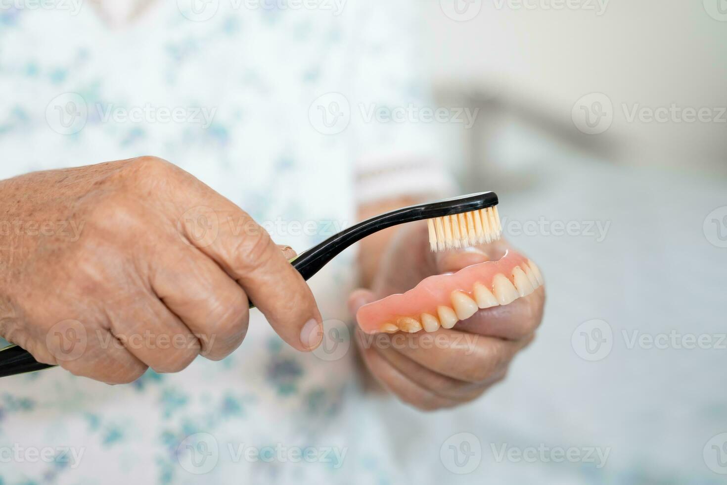 Asian elderly woman patient use toothbrush to clean partial denture of replacement teeth. photo