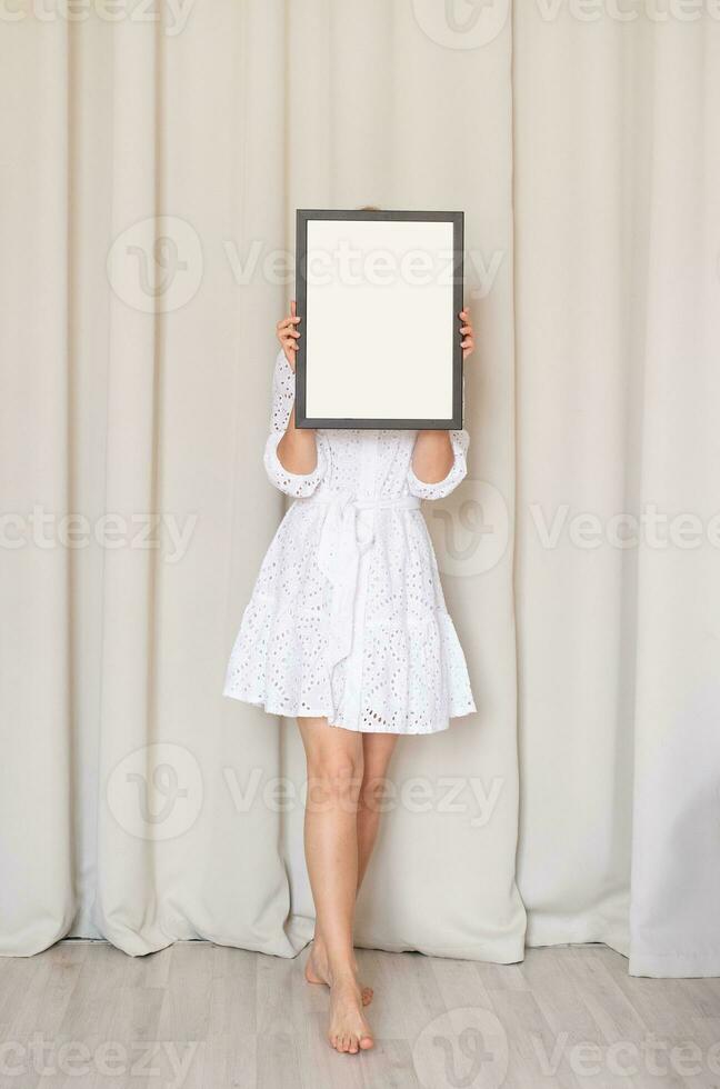 woman in dress holding blank frame, beige curtain background photo