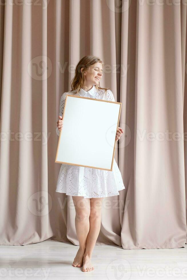 woman in dress holding blank frame, beige curtain background photo