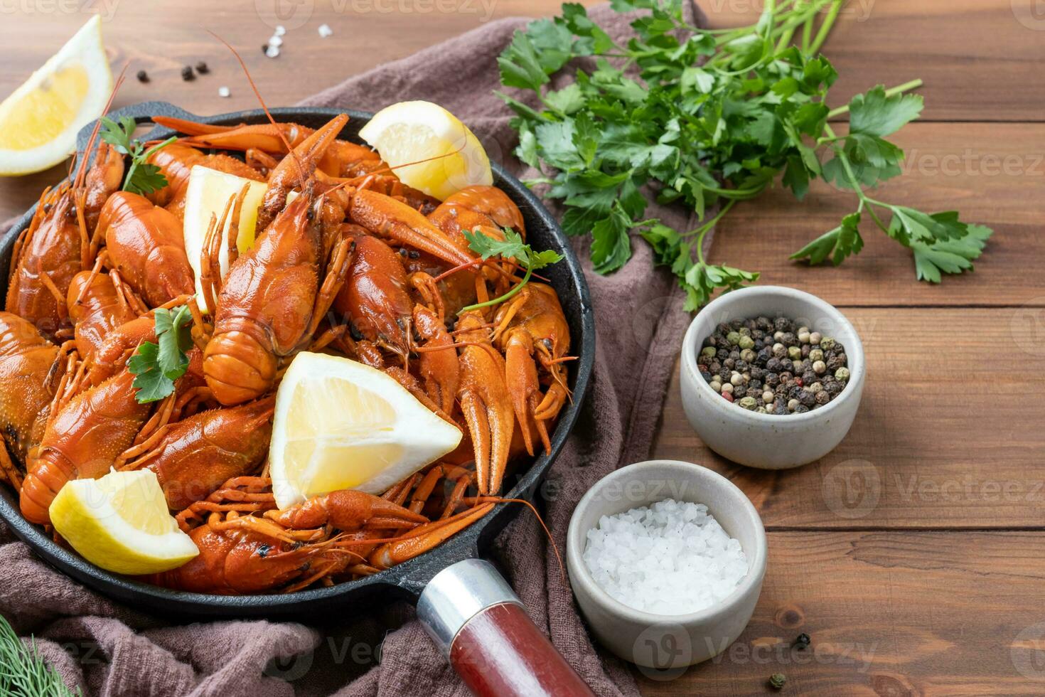 cooked crawfish in black saucepan with lemons and spices on wooden background photo