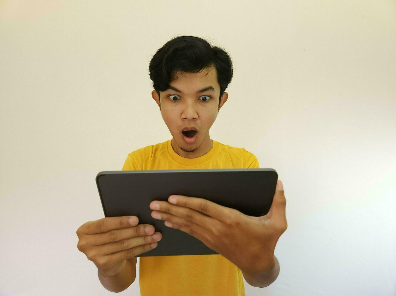 Surprised and excited asian man holding tablet isolated on white photo