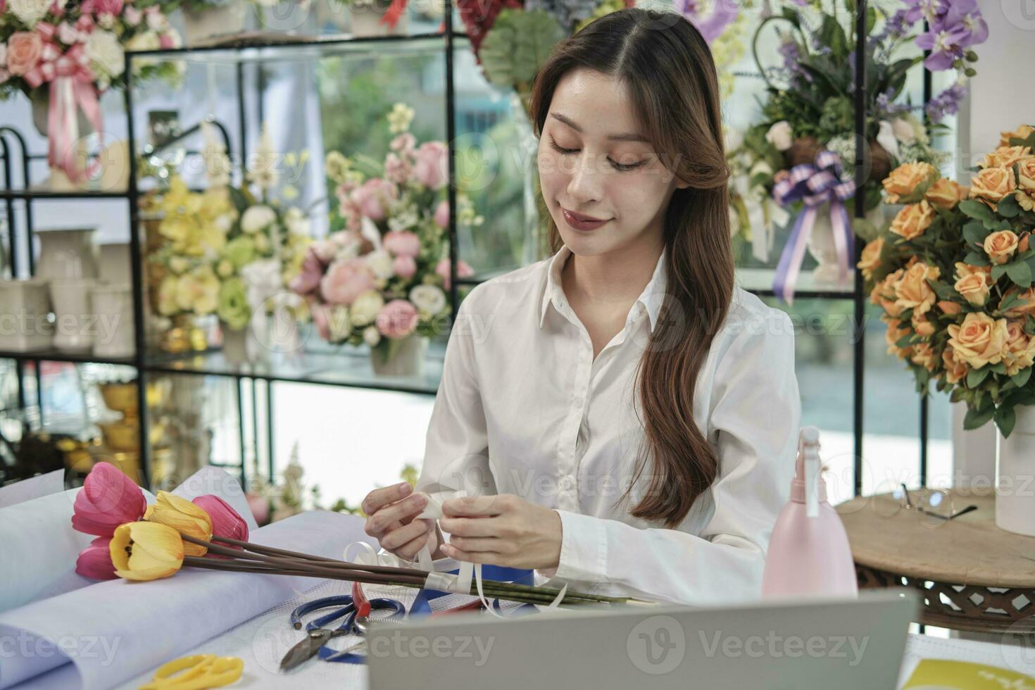 uno joven hermosa asiático hembra florista empresario arreglando un manojo de flores, decorando con encantador cintas, contento trabajo en vistoso flor tienda Tienda con flores, y pequeño negocio dueño. foto