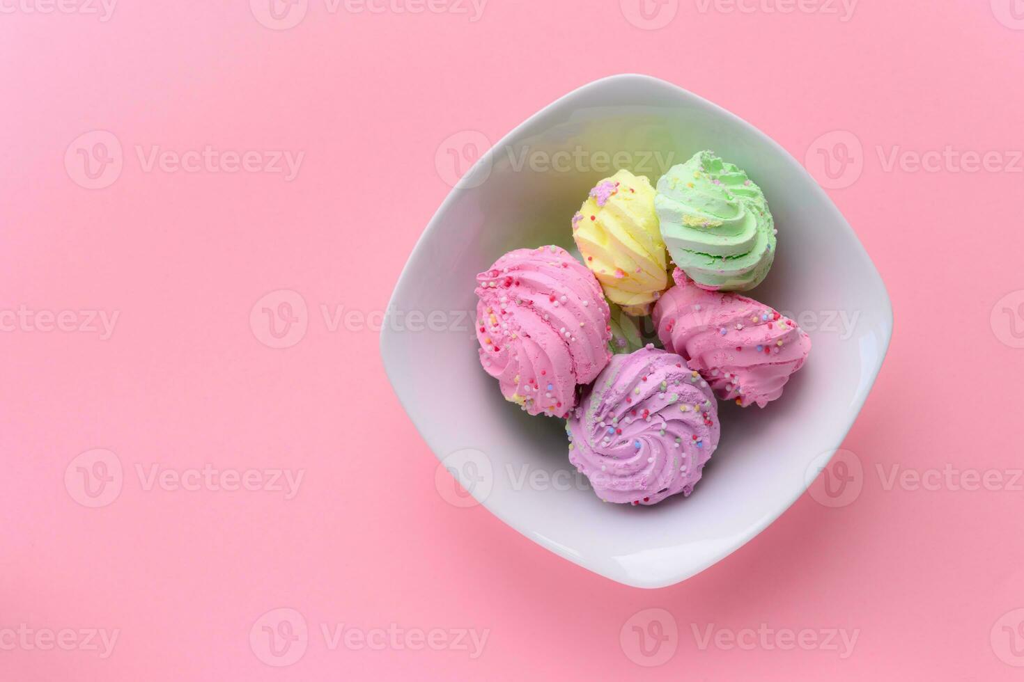 Colorful delicious meringues in white bowl on pink background copy space photo