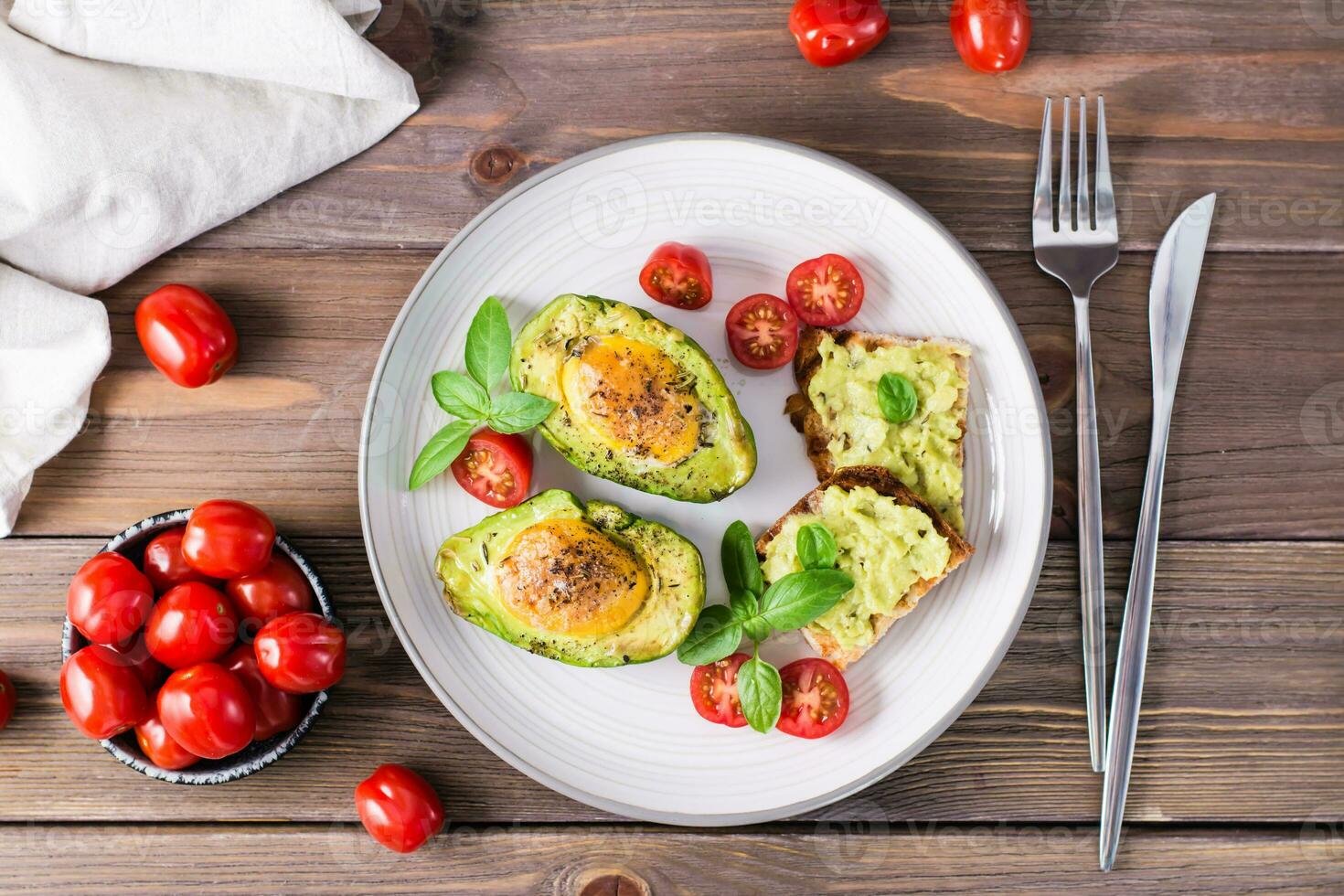 listo para comer aperitivo horneado aguacate con huevo, brindis y Cereza Tomates en un plato en un de madera mesa. sano comiendo. flexitariano dieta. parte superior ver foto