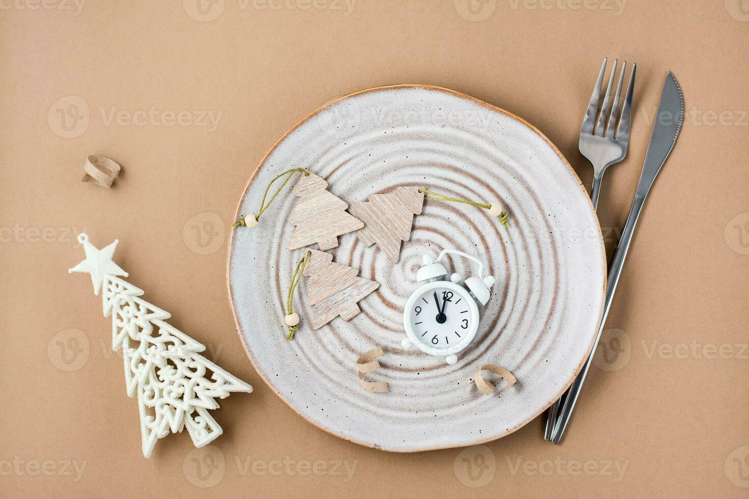 Concept Countdown on Christmas night. Table setting. Alarm clock and Christmas decorations on a plate on a beige background. Top view photo