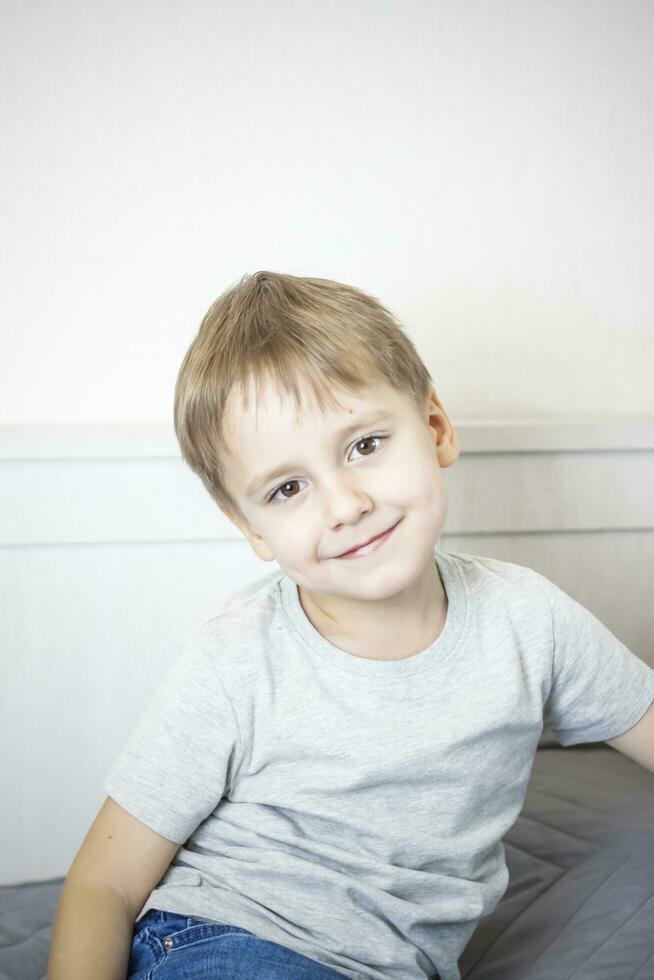 A photo of a handsome boy in a gray T-shirt looking at the camera. Portrait in a bright room. Natural, not staged photography.