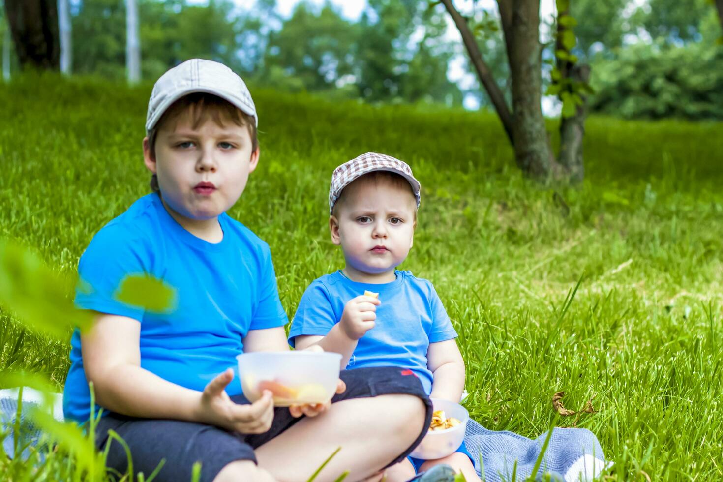 Summer and a warm day. Children on a picnic sit on a blanket and eat fruit from a plate. Live emotions of the guys. photo