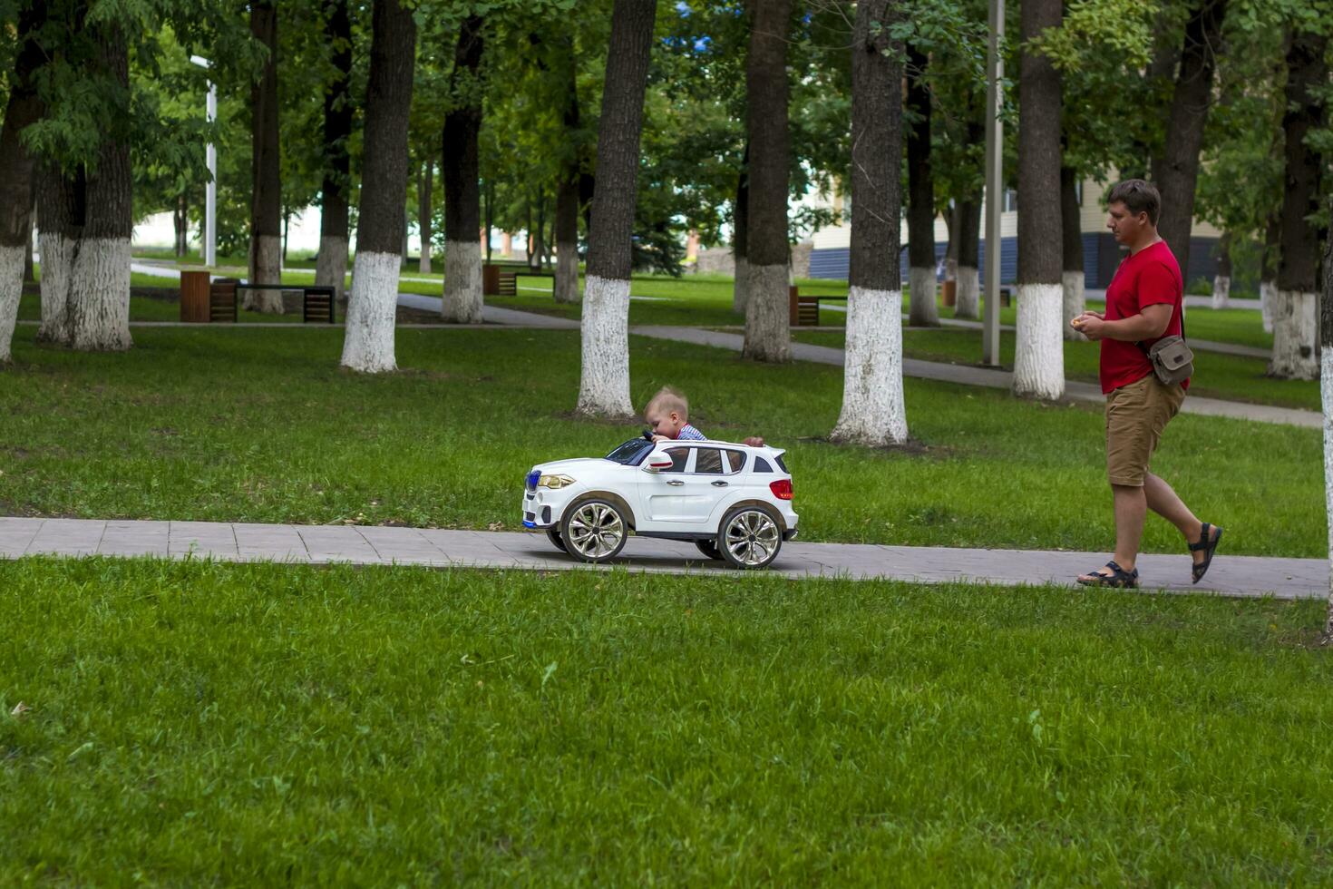 A small child is driven by a father in a children's car using a remote control. photo