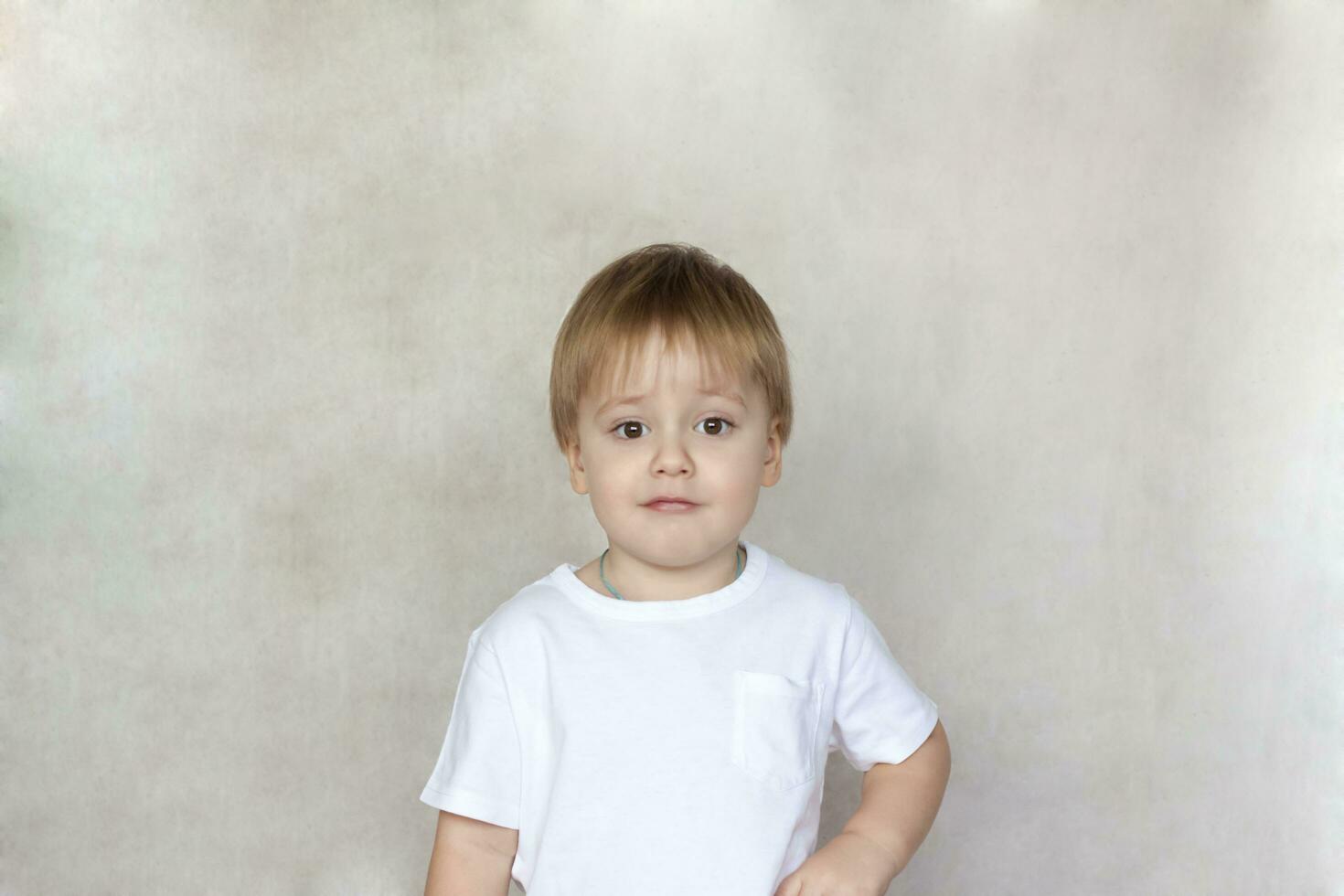 Portrait of a cute little boy in a white t-shirt. Children's emotions. Child on the background of the wall. Success, bright idea, creative ideas and concepts. photo