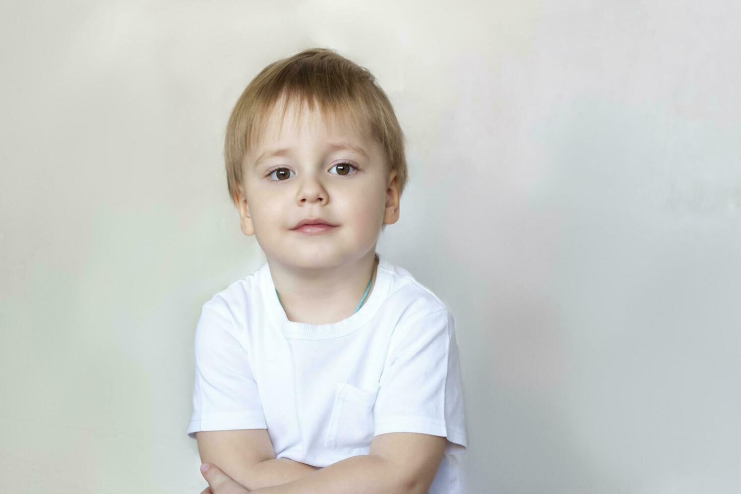 Portrait of a cute little boy in a white t-shirt. Children's emotions. Child on the background of the wall. Success, bright idea, creative ideas and concepts. photo