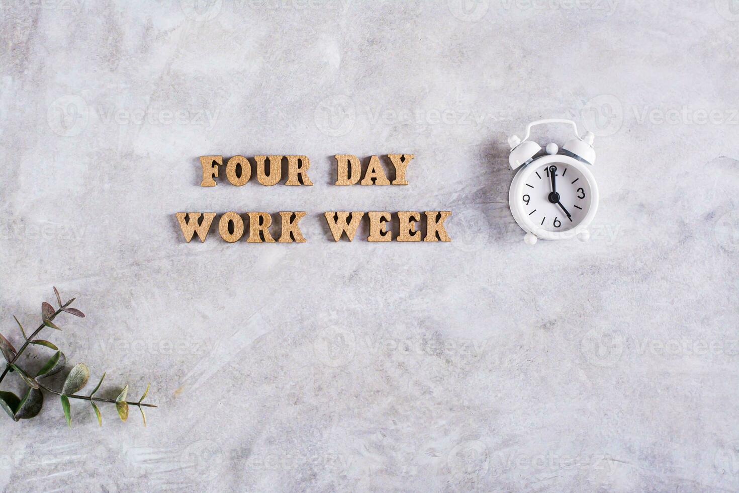 Four day work week concept with wooden letters and alarm clock on gray background photo