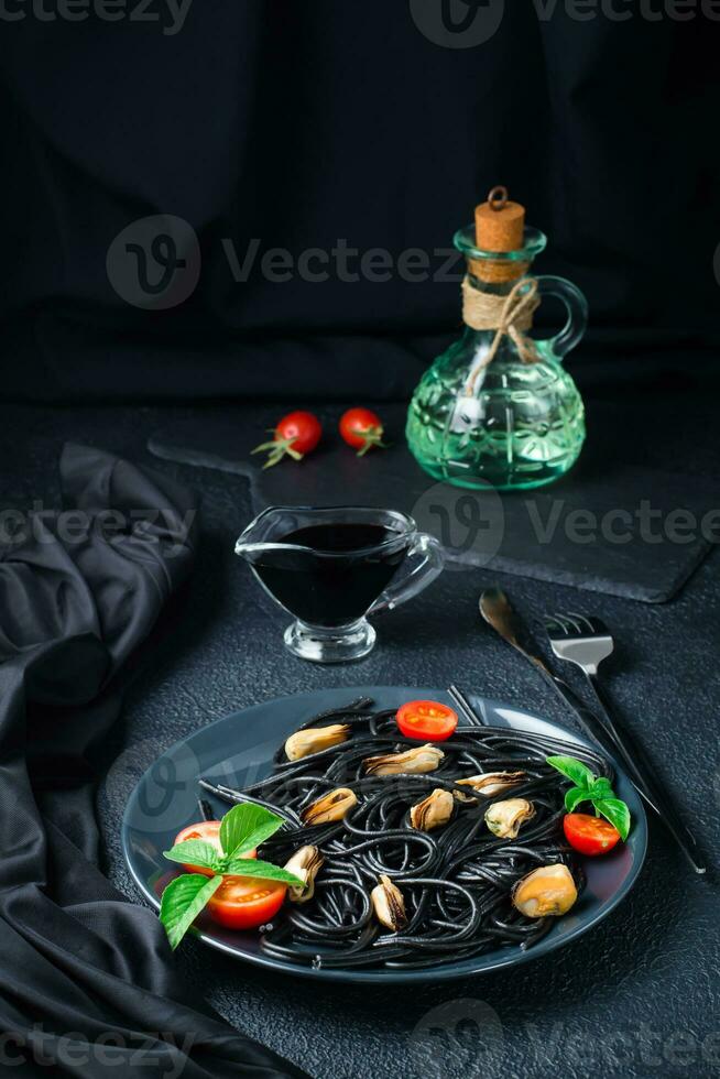 Ready-to-eat black spaghetti with mussels, tomatoes and basil on a plate on a black background. Food photography in dark colors. Vertical view photo
