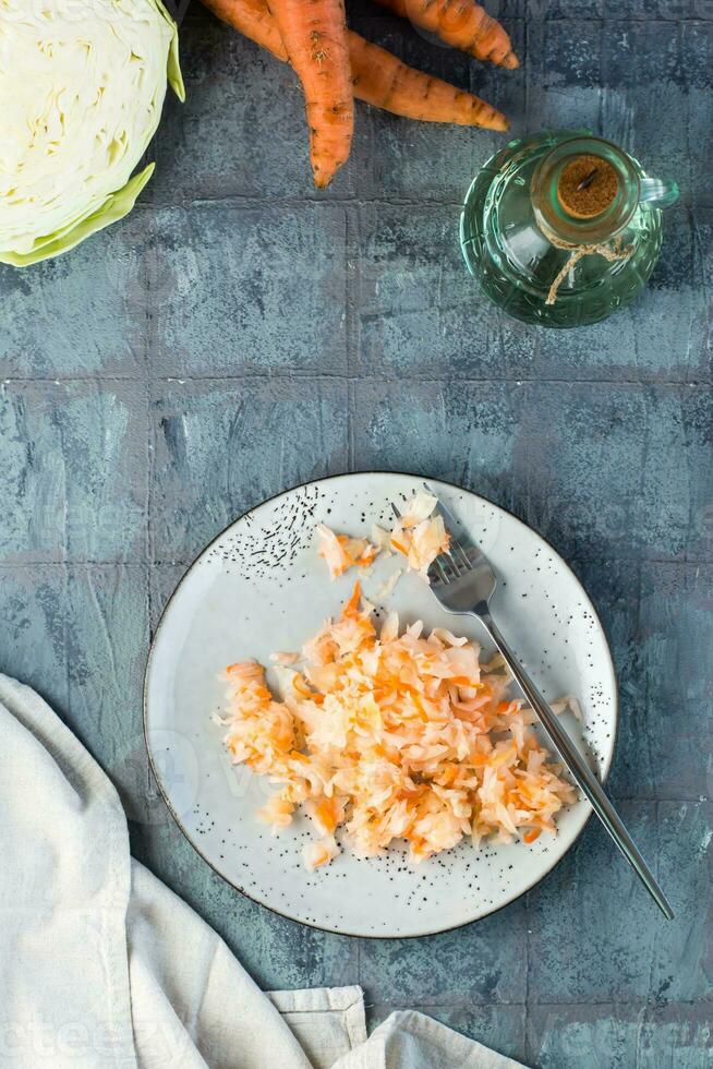 Fresco Chucrut con zanahorias y un tenedor en un plato en el mesa. fermentación y un vegetariano dieta. vertical y parte superior vista. foto