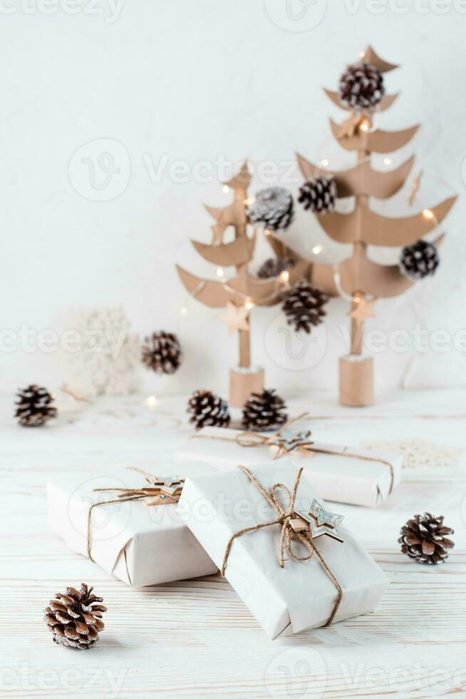 Christmas gifts wrapped in craft paper tied with twine on the background of Christmas fir trees made of cardboard on a wooden table. Organization of an eco-friendly holiday. Vertical view photo