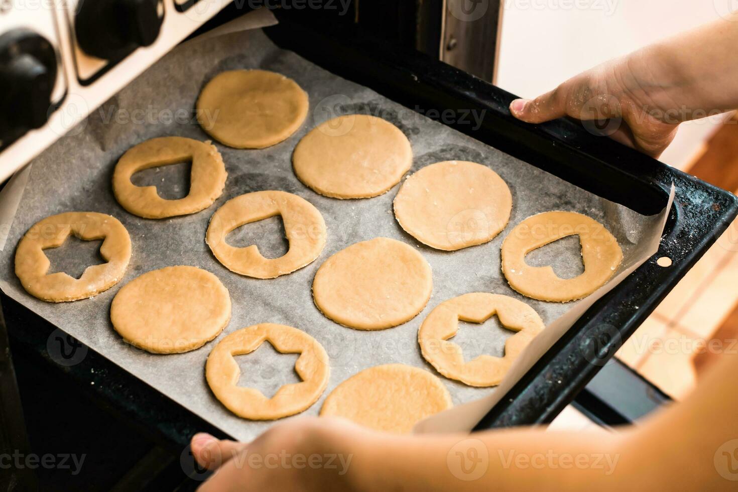 Hands insert a baking sheet of raw Linzer cookies into the oven. Cooking Christmas treats. Lifestyle photo