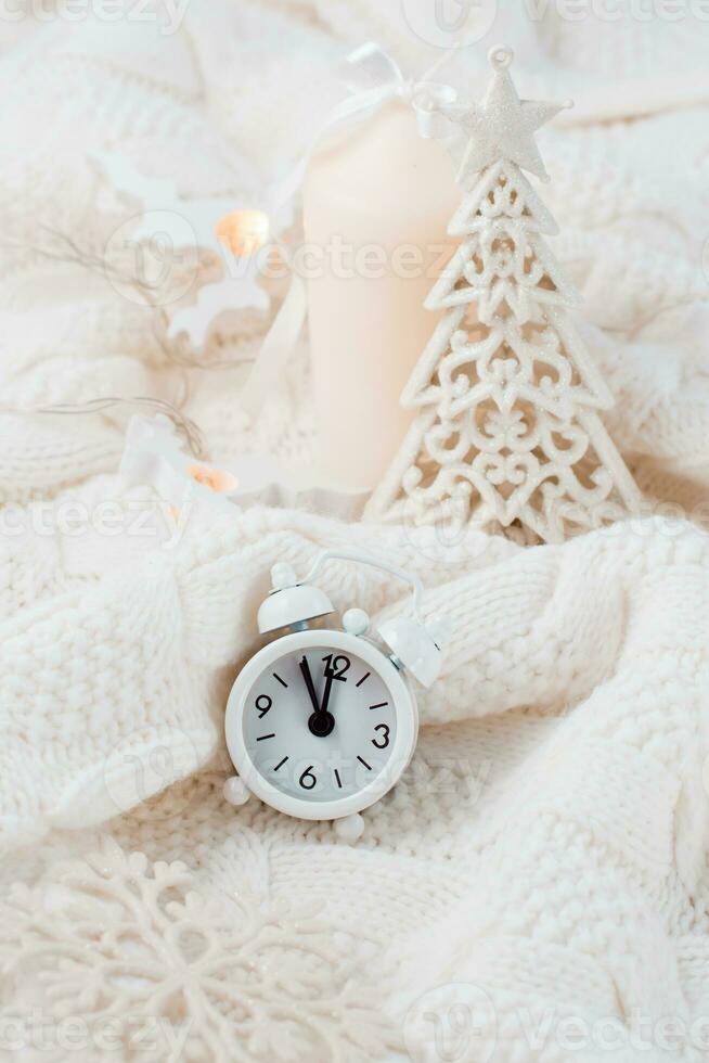 Countdown on Christmas night. Alarm clock, fir tree and candle on a knitted sweater. White colors. Vertical view photo