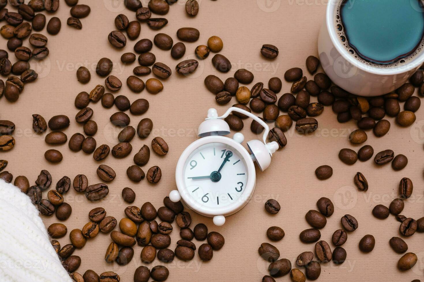 White alarm clock, a cup of black coffee and coffee beans on a beige background. Take a break from work to relax. Top view photo
