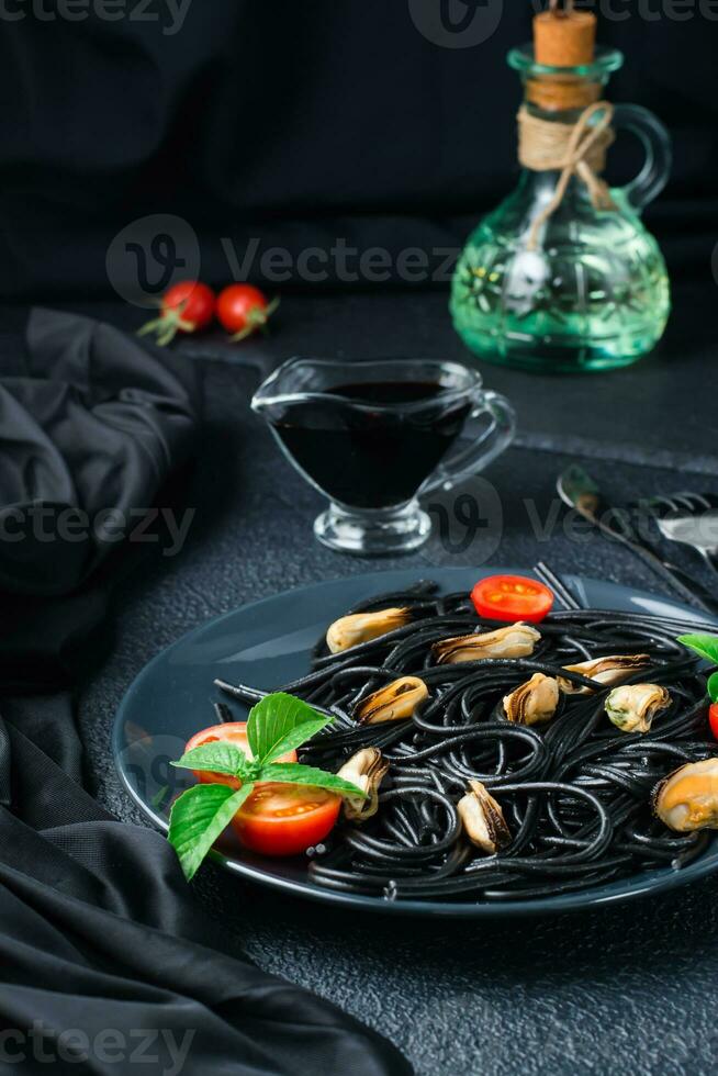Ready to eat black spaghetti with mussels, tomatoes and basil on a plate and soy sauce on a black background. Food photography in dark colors. Vertical view photo