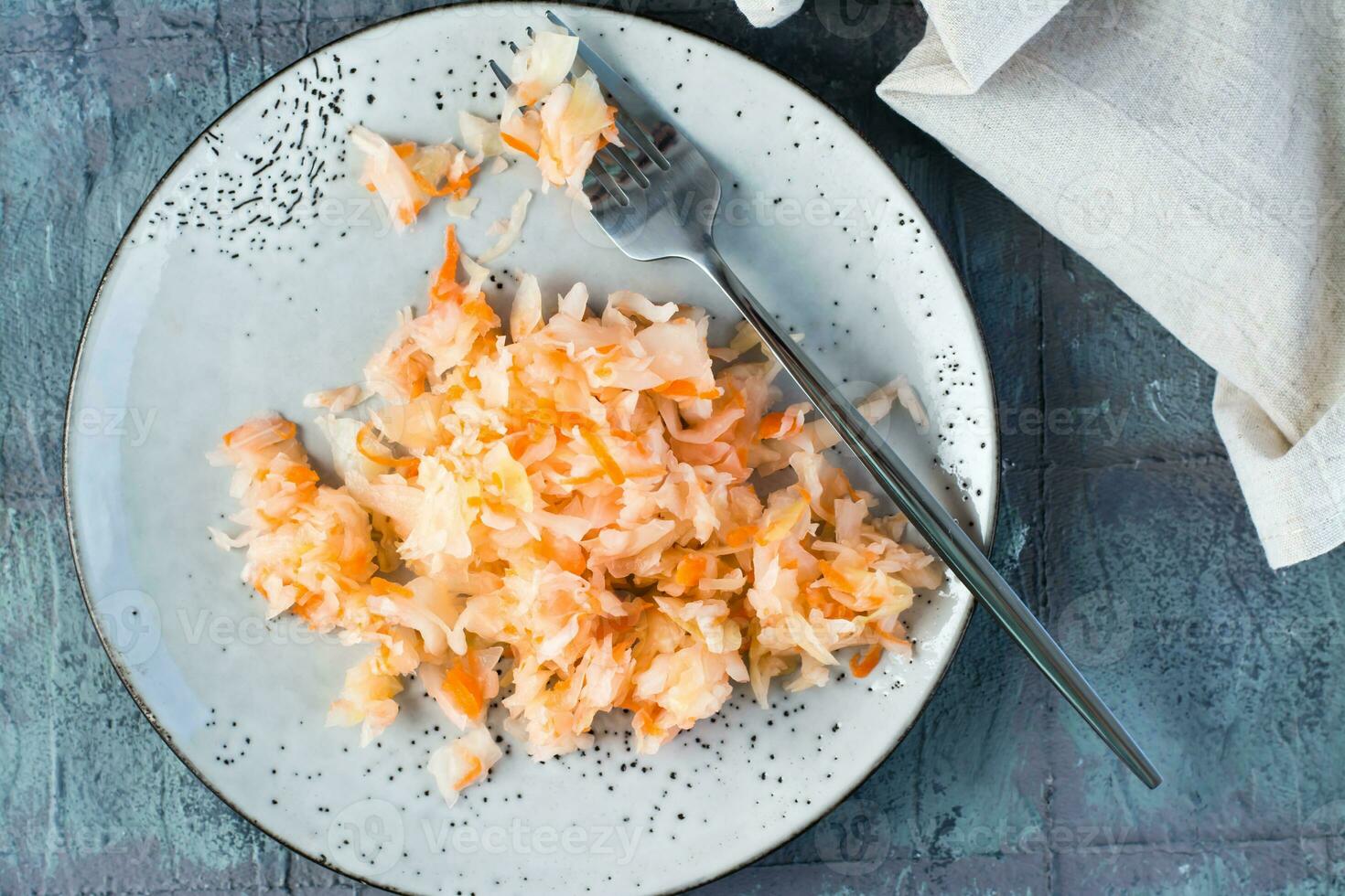 Fresco Chucrut con zanahorias y un tenedor en un plato en el mesa. fermentación y un vegetariano dieta. parte superior vista. de cerca foto