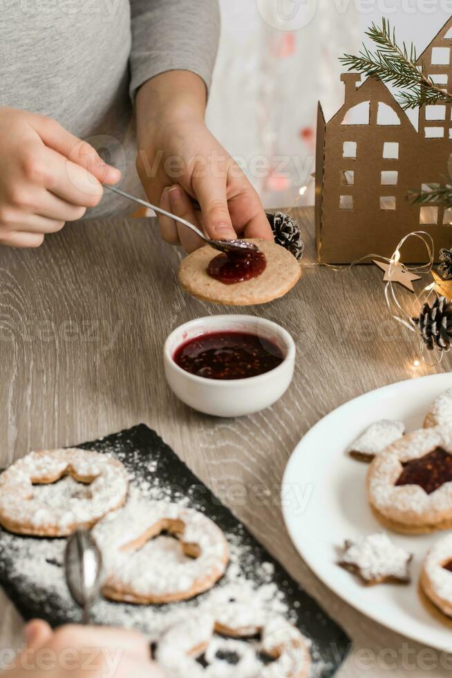 para niños manos untado baya mermelada en linzer galletas en el cocina mesa. Cocinando Navidad golosinas estilo de vida. vertical ver foto