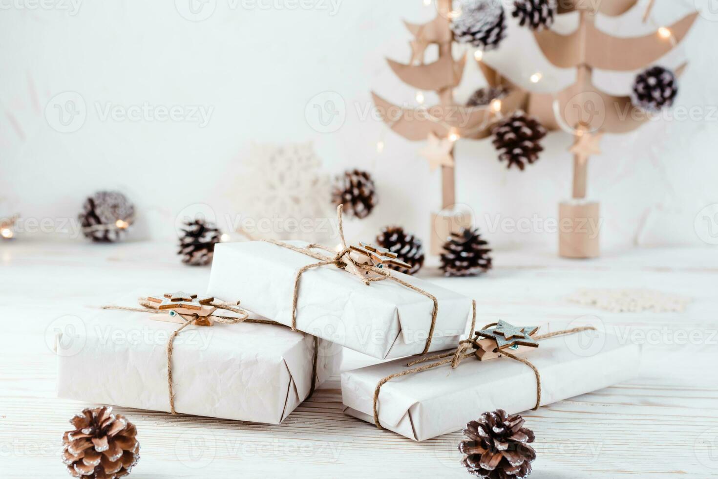 Ready-made Christmas gifts wrapped in craft paper tied with twine on the background of Christmas fir trees made of cardboard on a wooden table. Organization of an eco-friendly holiday photo