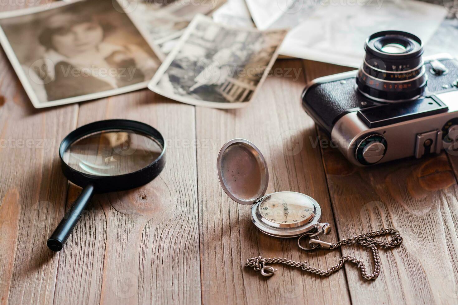 Antique watch on a chain, magnifier, film camera and black and white photographs on a wooden table. Nostalgia for the past. Time concept photo