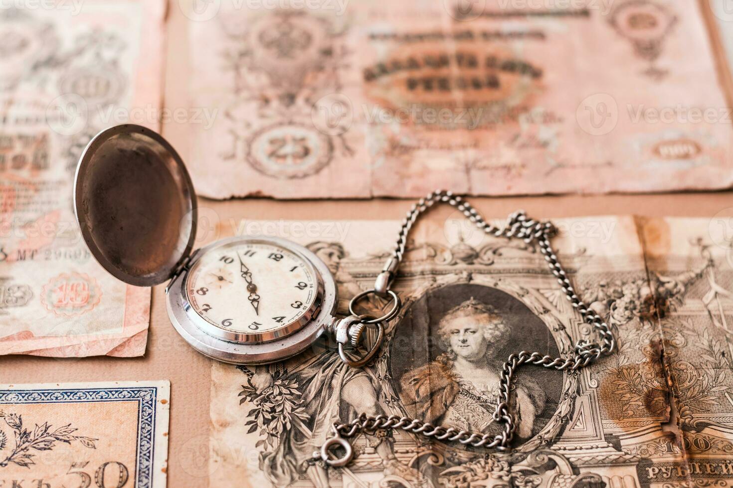 Old worn out of circulation ruble banknotes of tsarist russia and a watch on a chain on a brown background photo