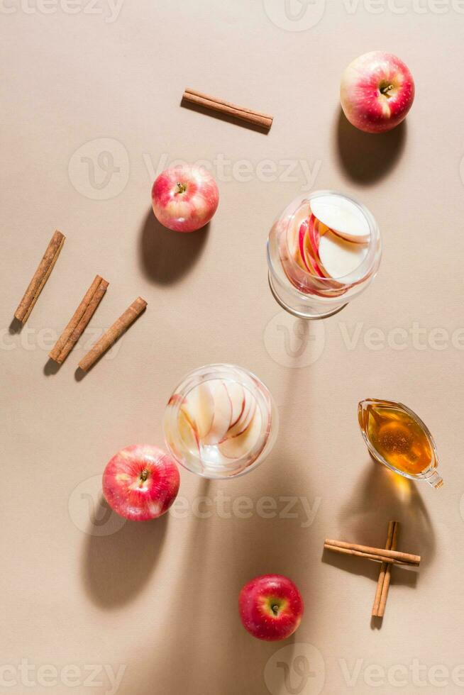 Refreshing cocktail of apple pieces and mineral water in glasses, honey and cinnamon on a brown background in harsh light. Detox wellness drink. Top view photo