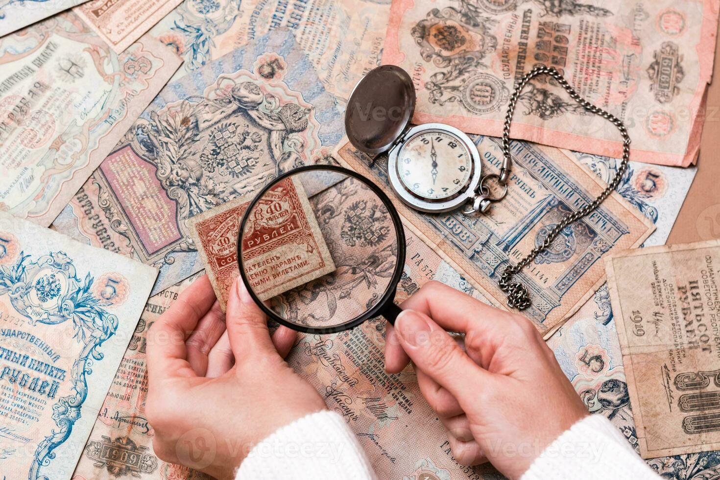A woman holds a magnifying glass in her hands and examines old ruble banknotes out of circulation. photo