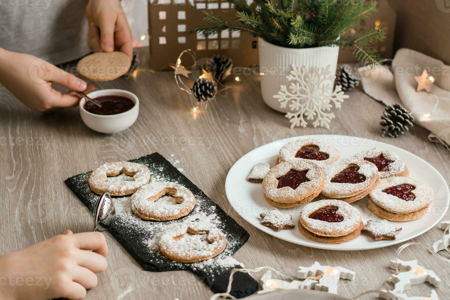 Children grease Linzer cookies with berry jam on the kitchen table. Cooking Christmas treats. Lifestyle photo