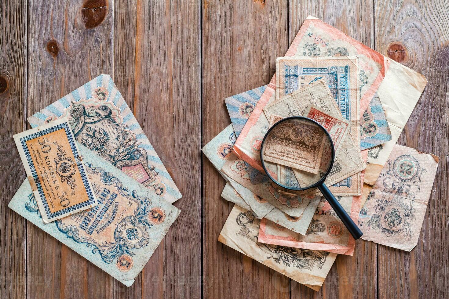 The magnifying glass lies on a pile of old ruble banknotes out of circulation on a wooden table. Study of history. Top view photo