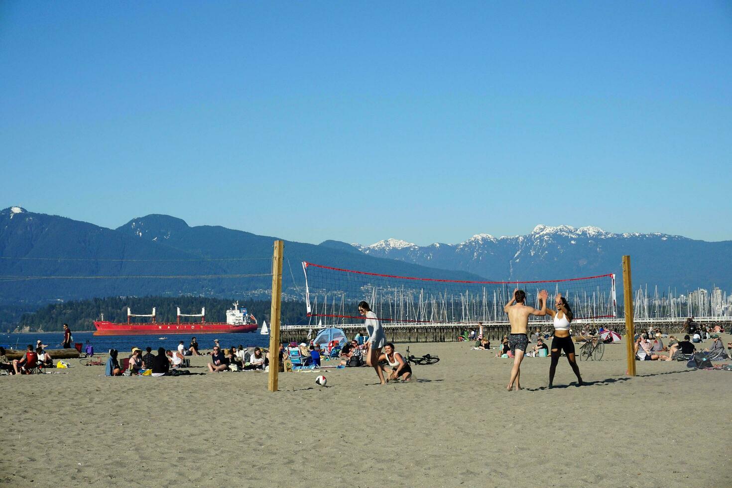 People enjoyng the beach on sunny day. Beautiful snow mountains and ocean on background. Vancouver, BC, Canada. Jericho Beach. April 18, 2021 photo