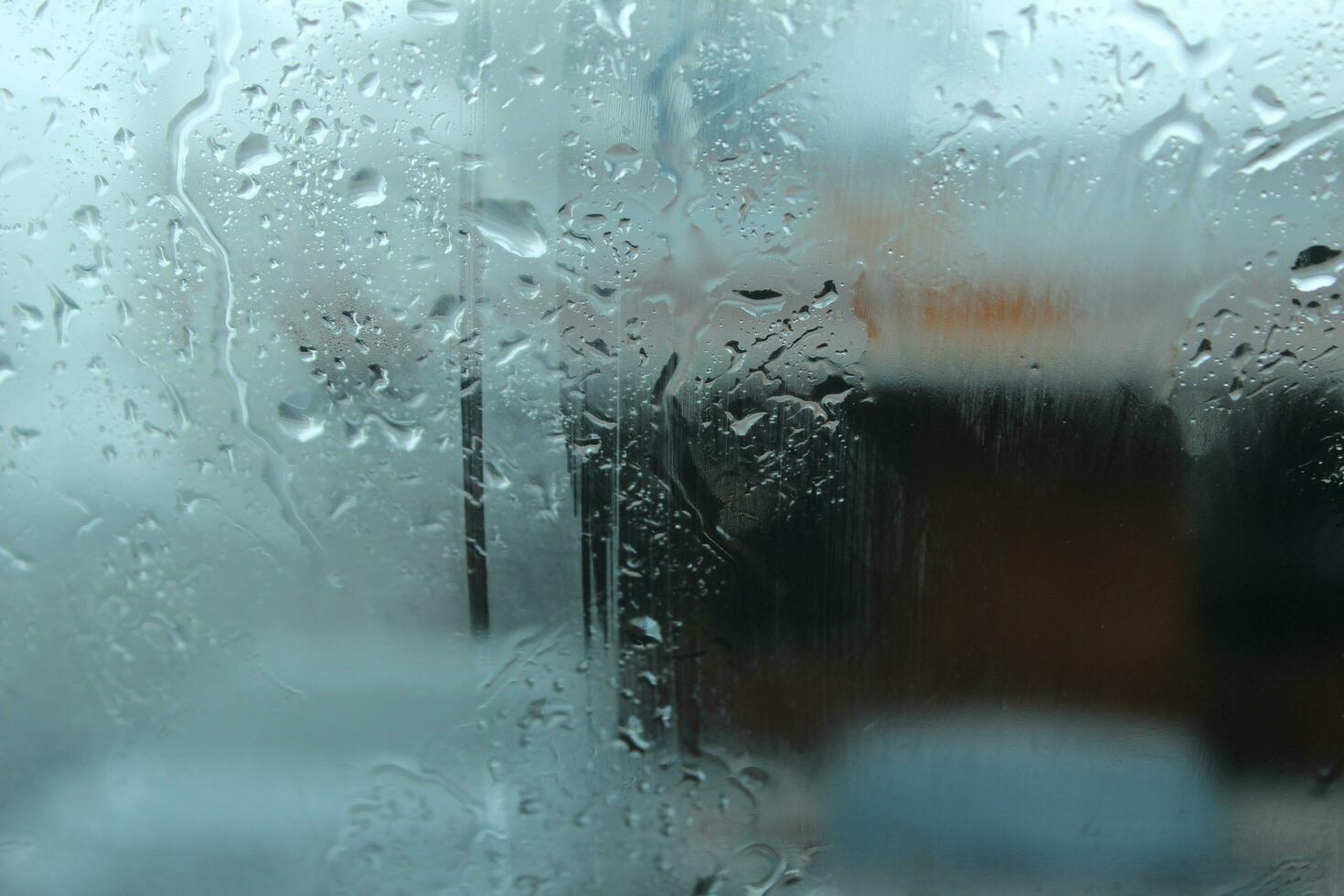 A close-up of the wet glass window of a motor vehicle, with raindrops and snow falling in the freezing indoor backgrounds. photo