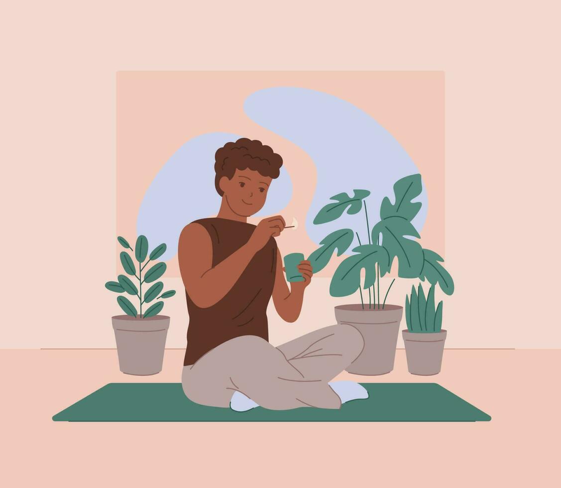 Black man sits on a yoga mat and lights a candle on the background of beautiful plants vector