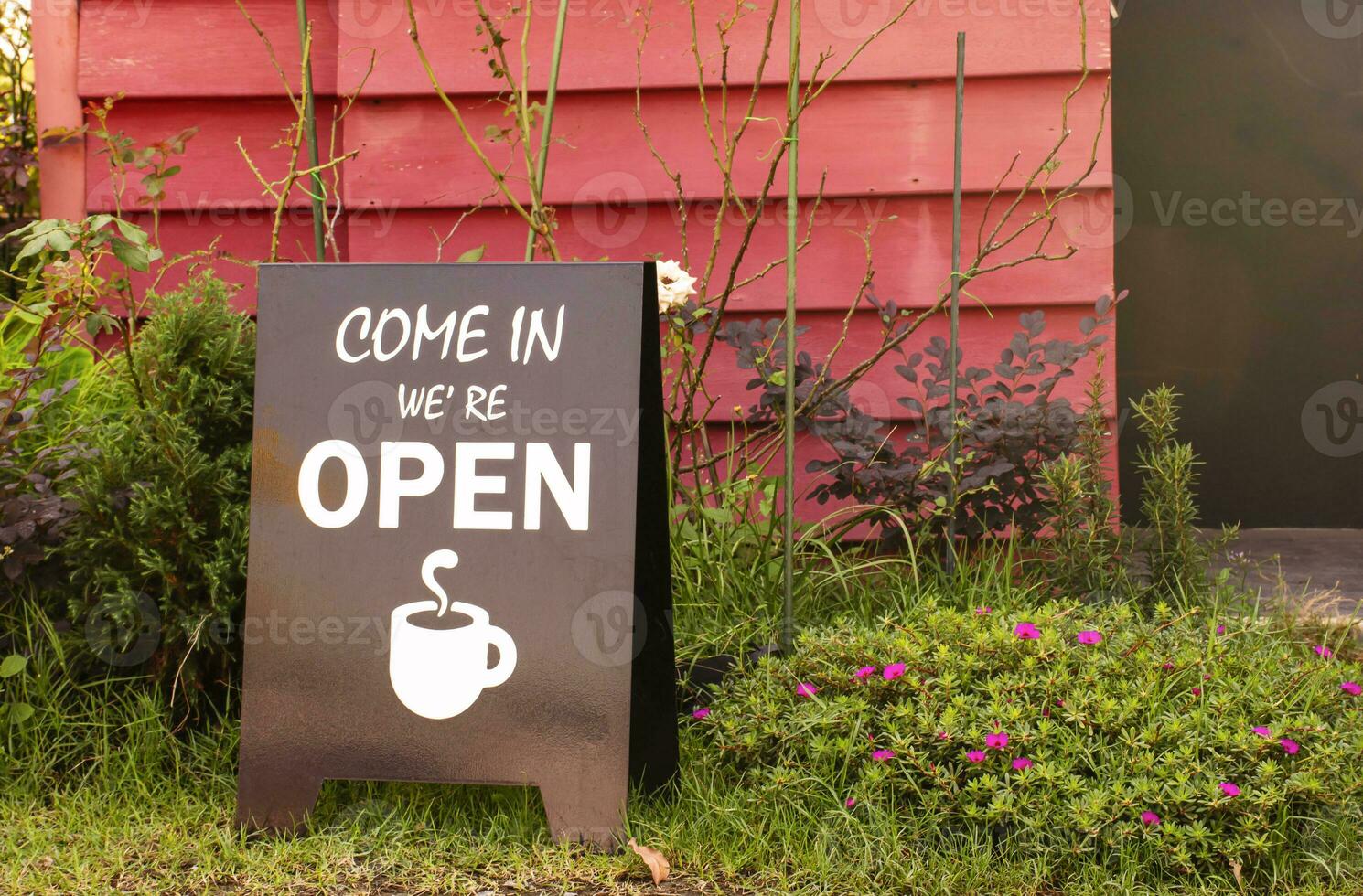 Brown sign with message COME IN WE'RE OPEN and icon coffee cup on glass at entrance coffee shop photo