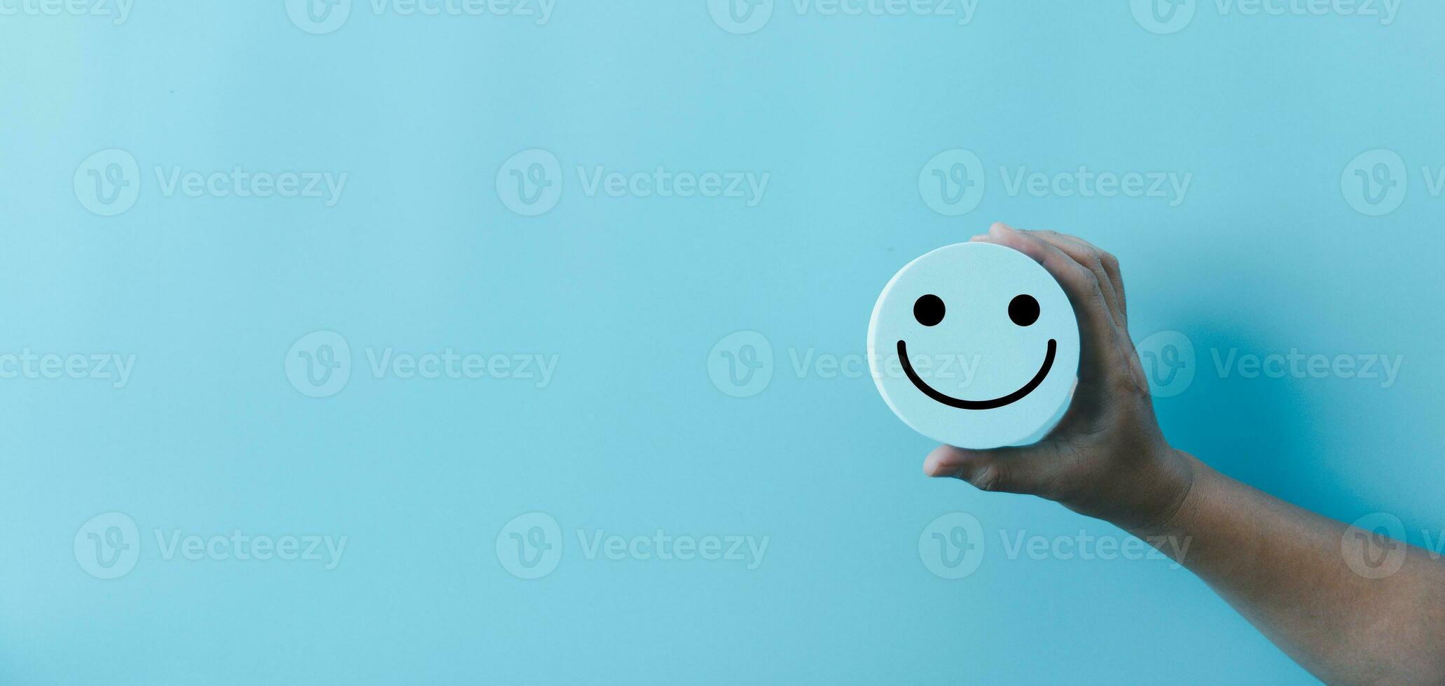 Woman hand holding happy face smile face icon on round blue object. Customer experience and service with satisfaction concept. positive thinking, mental health assessment, world mental health day. photo