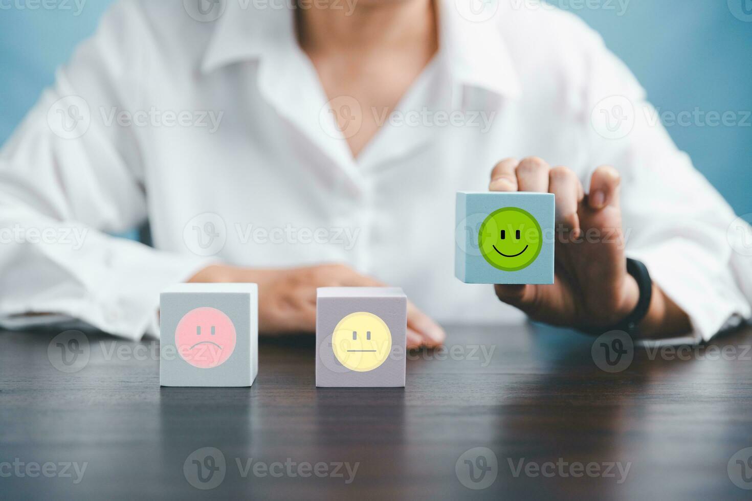 Woman hand holding happy face smile face icon on cube blue object. Customer experience and service with satisfaction concept. positive thinking, mental health assessment, world mental health day. photo