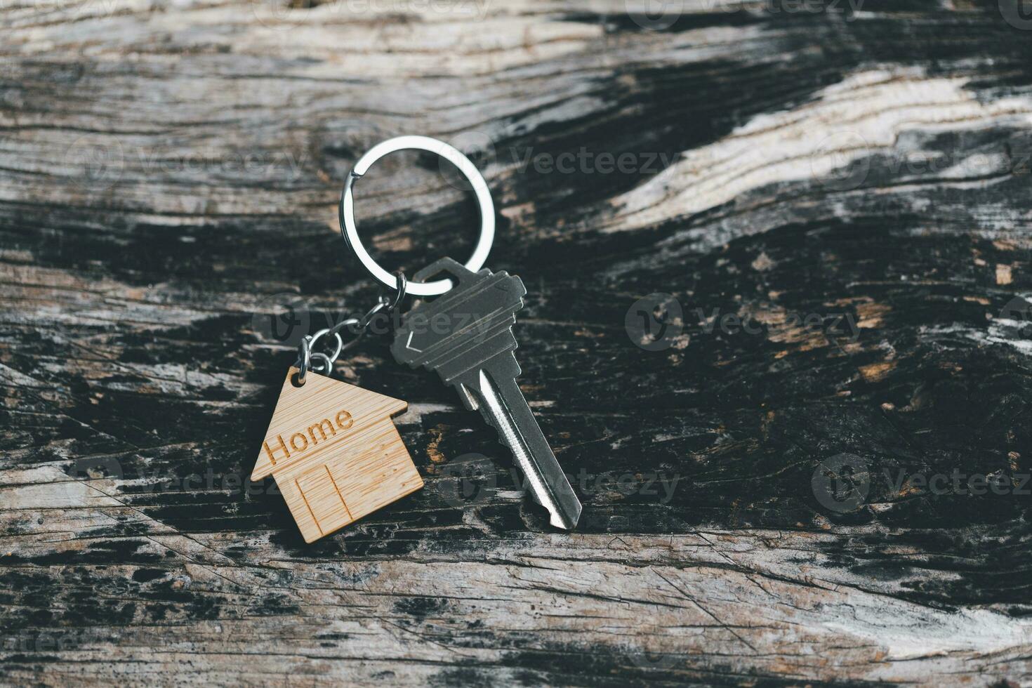 House key on a house shaped keychain resting on wooden floorboards concept for real estate renting property. House model and key in house door. Real estate agent offer house, property insurance. photo