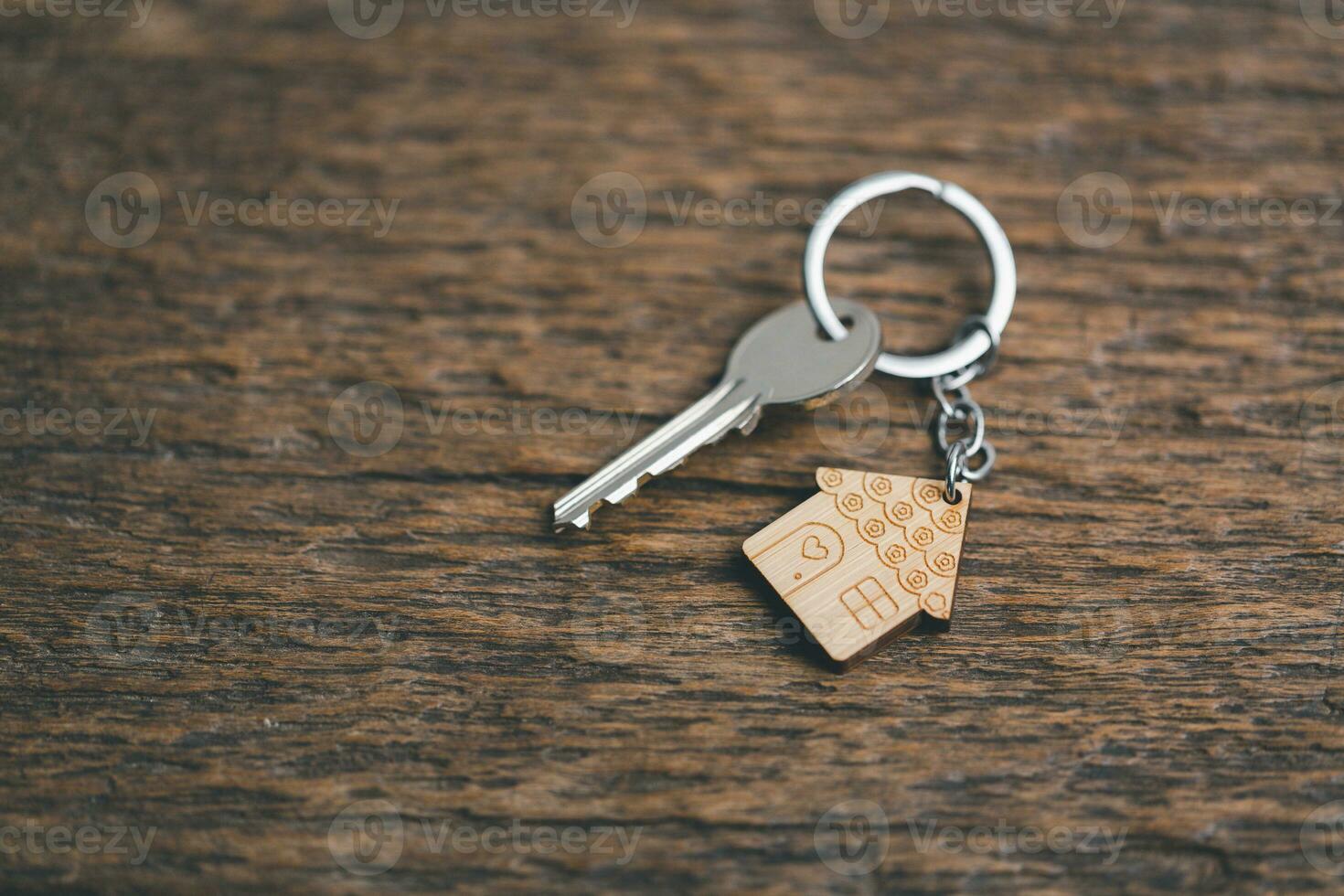 House key on a house shaped keychain resting on wooden floorboards concept for real estate renting property. House model and key in house door. Real estate agent offer house, property insurance. photo