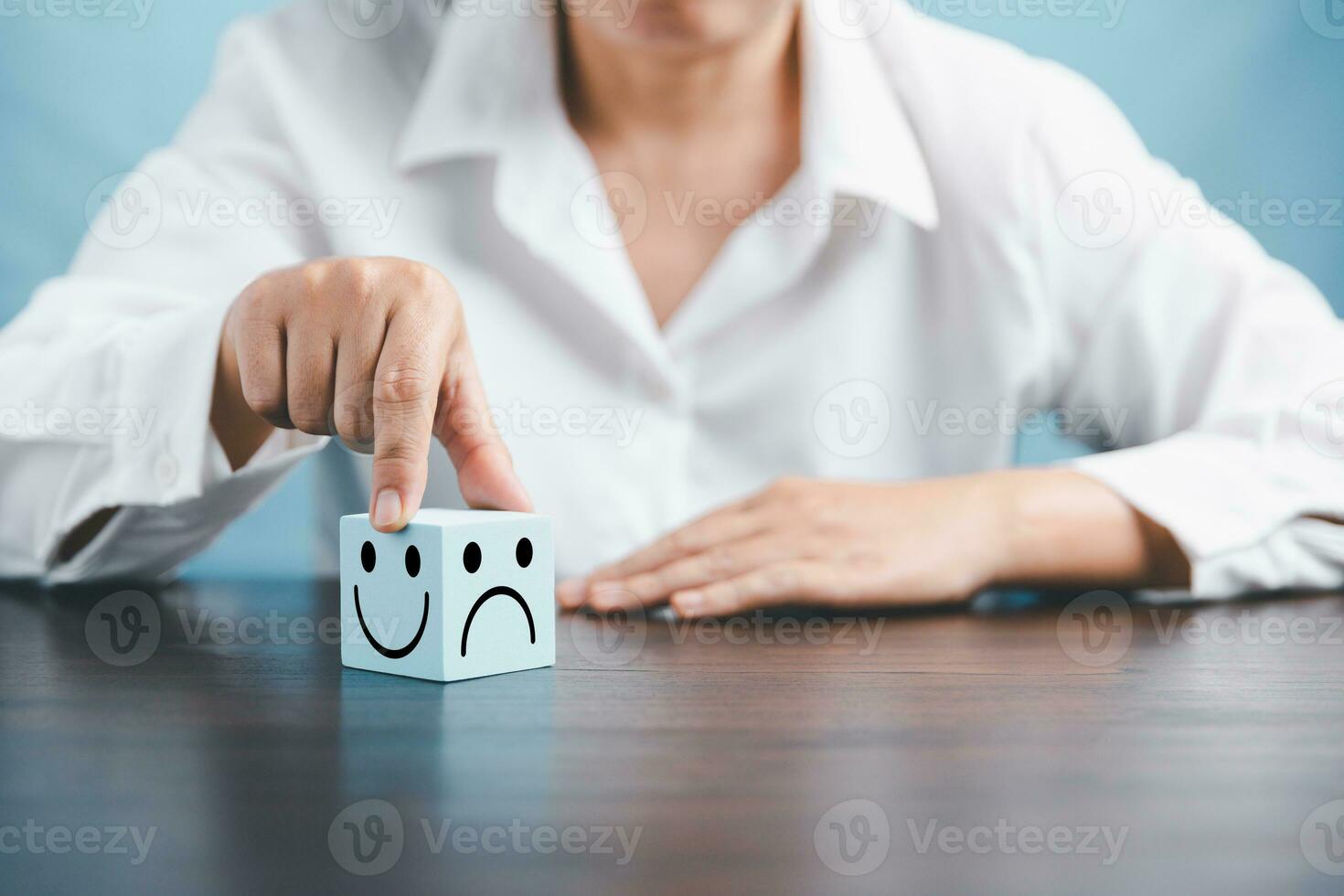 Woman hand holding happy face smile face icon on cube blue object. Customer experience and service with satisfaction concept. positive thinking, mental health assessment, world mental health day. photo
