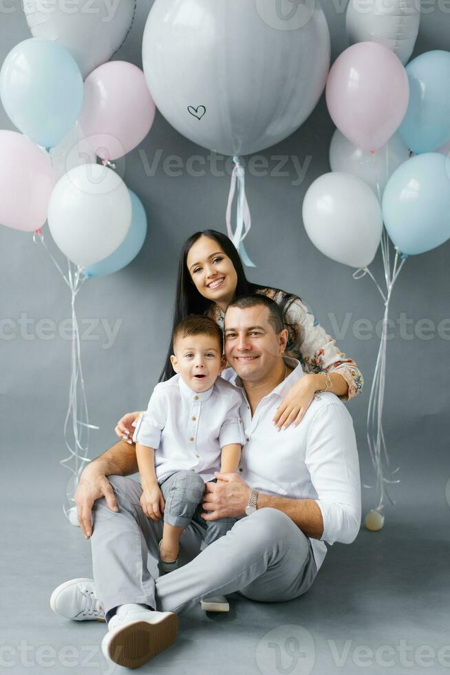 A young stylish family waiting for their second child against the background of a pop ball to determine the sex of the unborn child. Parents with their eldest son on a gray background photo
