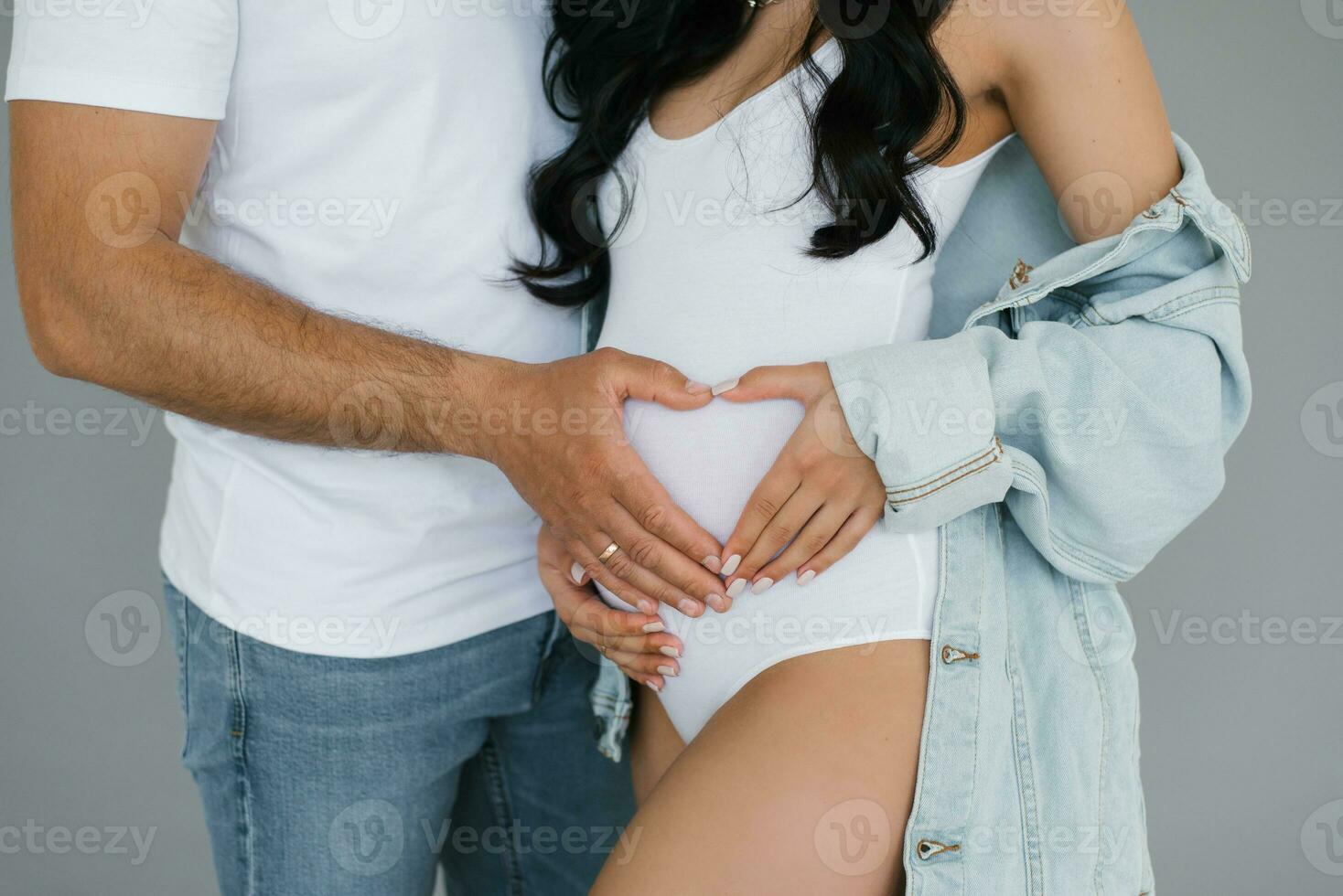 un joven casado Pareja es esperando para el nacimiento de un niño. el futuro padre toques su de la esposa embarazada barriga y sostiene su manos en el formar de un corazón foto