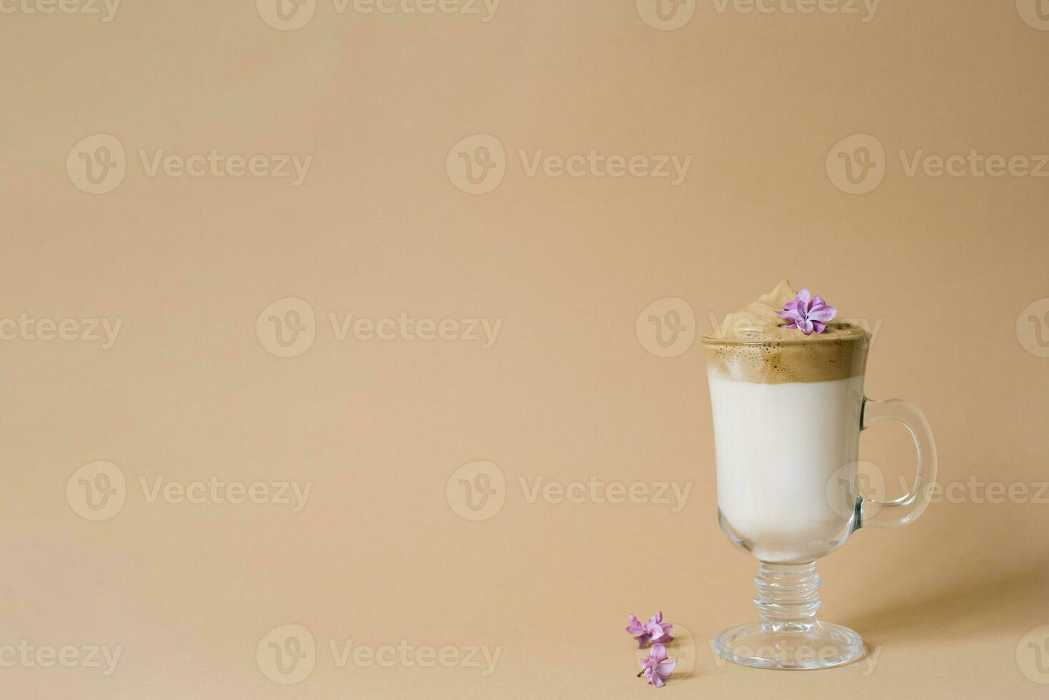 Beautiful dalgon coffee drink with foam in a transparent Cup and lilac flowers on a beige background. Copy space photo