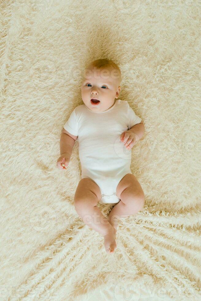 Cute charming white Caucasian boy with blue eyes lying on the bed smiling at the camera. View from above. A happy lifestyle in childhood. photo