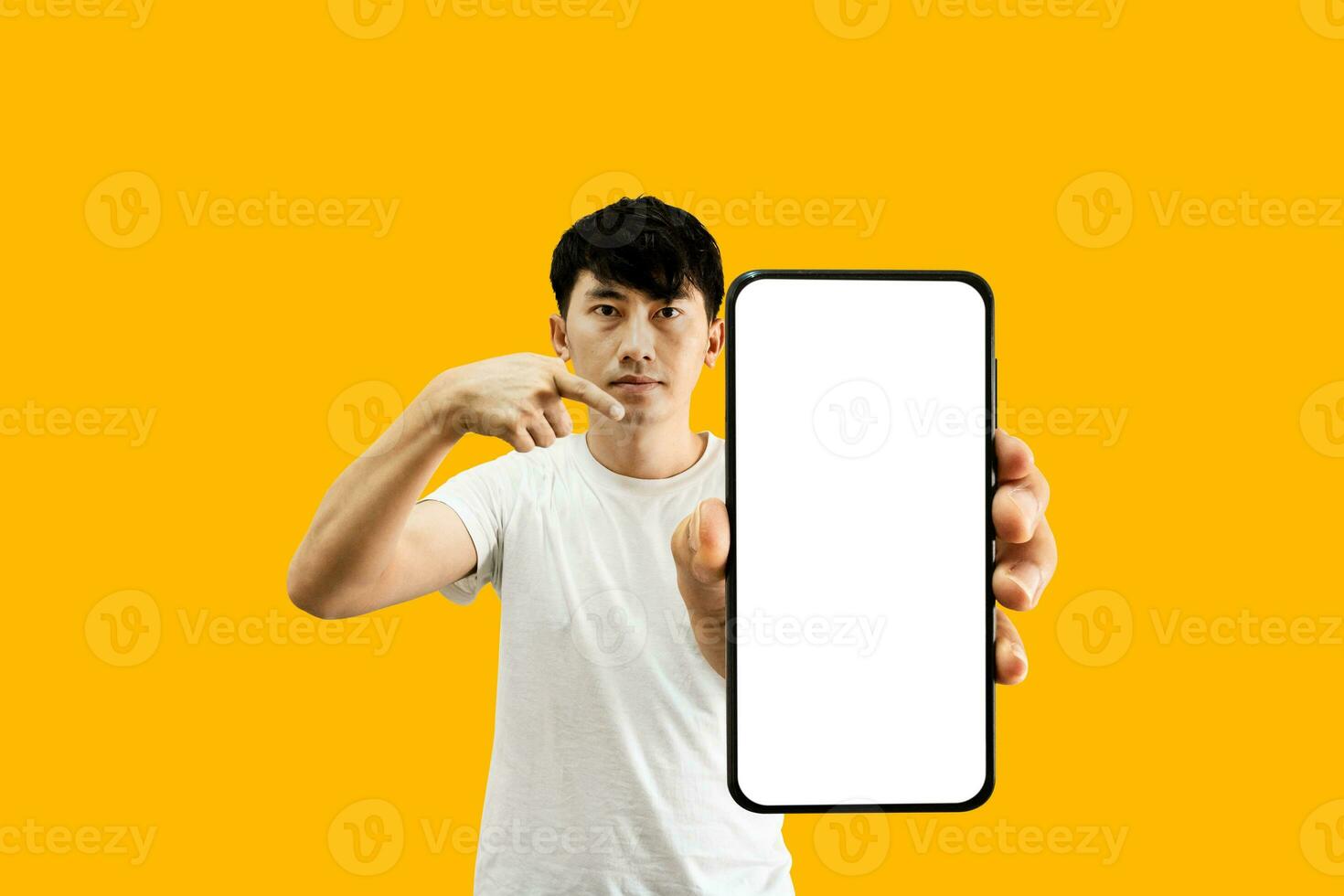 Asian Man Holding Smartphone With White Empty Screen On Yellow Background. Cellphone display Mockup for Mobile App Advertisement. photo